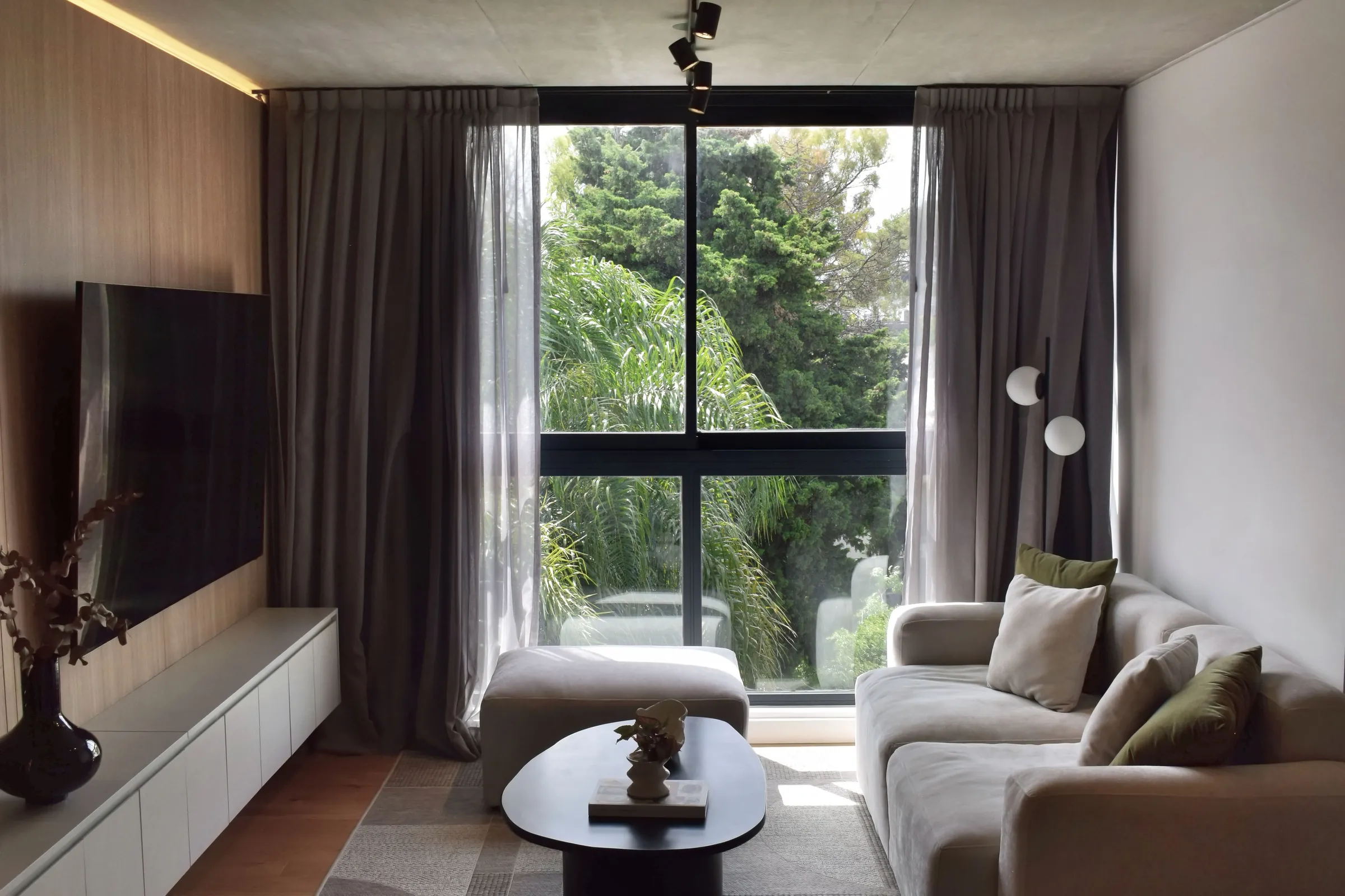 Living del proyecto Núñez: revestimiento de madera, sillón claro y un ventanal hacia el verde